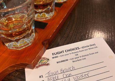 A wooden flight board at Red Pines Onalaska holds four glasses of bourbon on a table beside a menu listing Town Branch, Noble Oak, Kentucky Walker, and Penelope. The note section is blank, awaiting your thoughts.